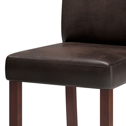A close-up of the Acadian - Upholstered Parson Dining Chair (Set of 2) shows its dark brown leather, cushioned seat, wooden legs, and a partially visible backrest.