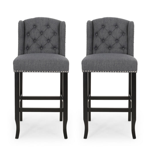 The Vienna - Contemporary Fabric Tufted Wingback Counter Stools (Set of 2) feature dark wooden legs, diamond-tufted gray fabric backs, and silver nailhead trim, shown side by side against a white background.