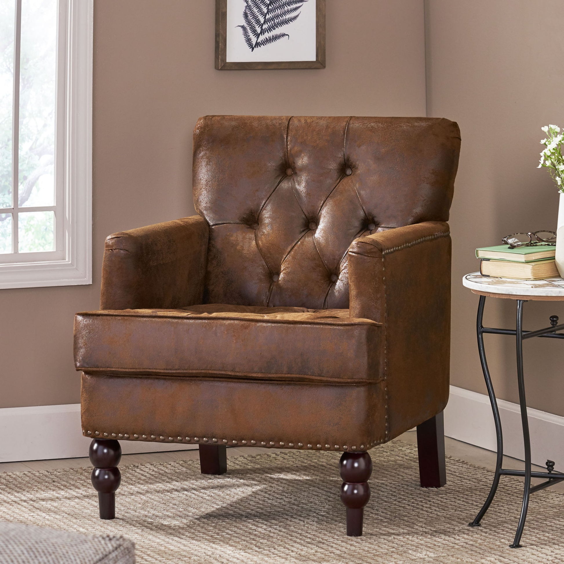 The Vitality Club Chair, featuring button tufted diamond stitching and turned wooden legs, sits on a beige carpet near a side table with books and flowers by a window in a cozy, naturally lit room.