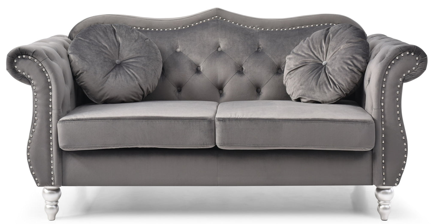 The Stylish Flared Arm Loveseat features a gray velvet finish, tufted backrest, silver nailhead trim, rolled arms, two matching round pillows, silver legs, and a classic, elegant design.