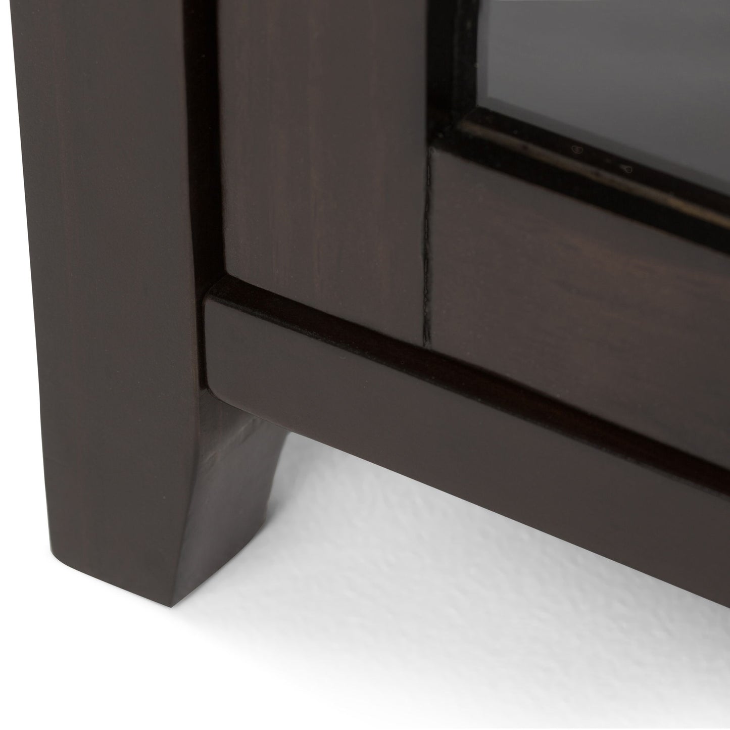 Close-up of the bottom corner of the Cosmopolitan - Handcrafted Medium Storage Cabinet, featuring dark wood and a glass panel, resting on a white surface.
