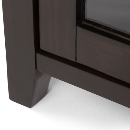 Close-up of the bottom corner of the Cosmopolitan - Handcrafted Medium Storage Cabinet, featuring dark wood and a glass panel, resting on a white surface.
