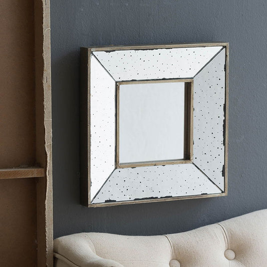 The Distressed Accent Mirror, a traditional style framed wall mirror, hangs on a gray wall above a light beige upholstered couch. Part of a wooden shelving unit is visible on the left.