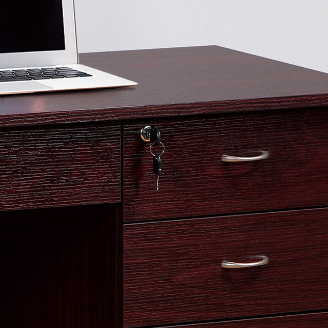 A Three Locking Drawers On Metal Glides Student Desk with mahogany finish features metal bar handles, a laptop on top, and a key in the lock of the top drawer. Two more drawers are visible below, with a modesty panel for added privacy.