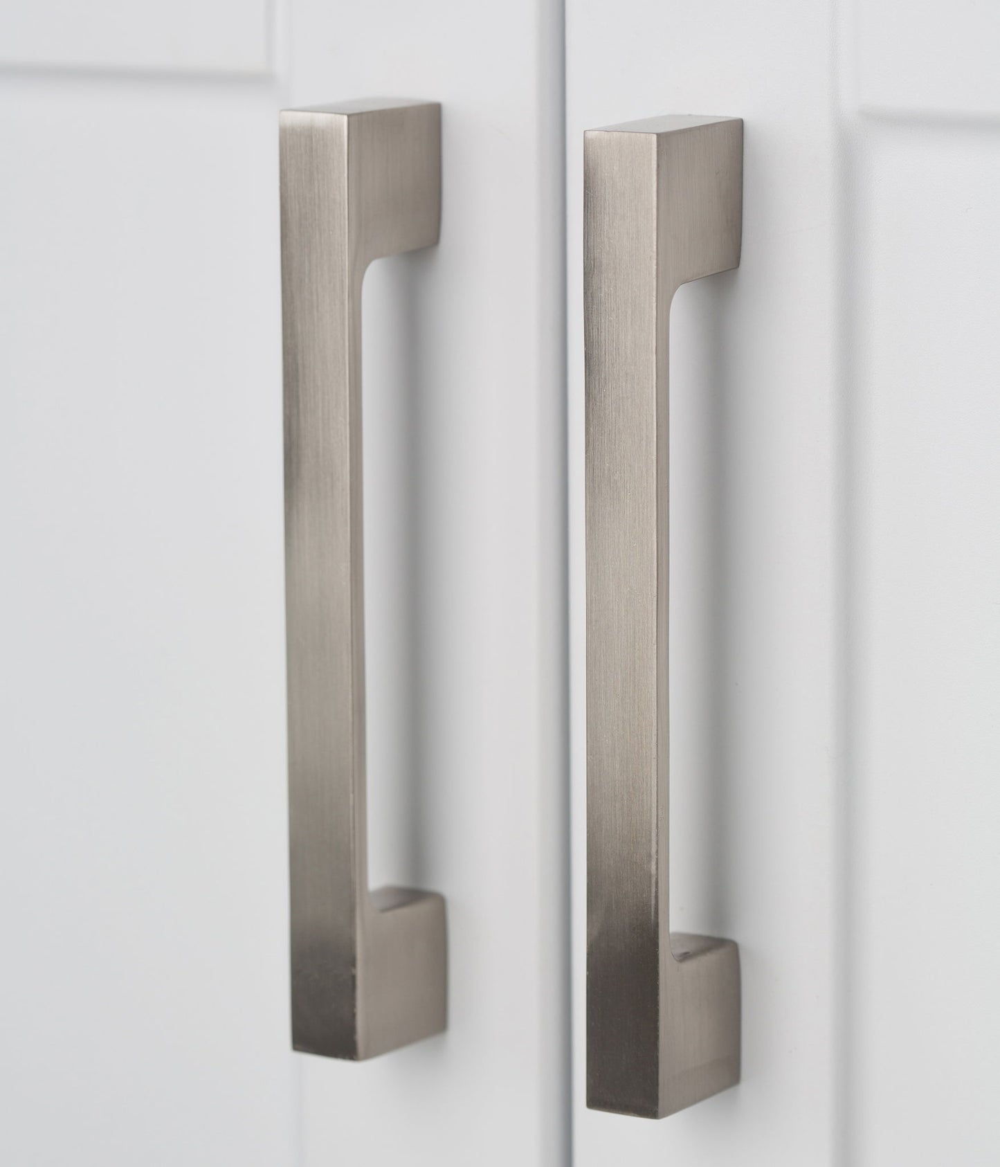 Two modern, rectangular brushed metal handles are mounted vertically on the white doors of the Hennessy - Deluxe Laundry Cabinet With Faucet And Stainless Steel Sink, positioned side by side.