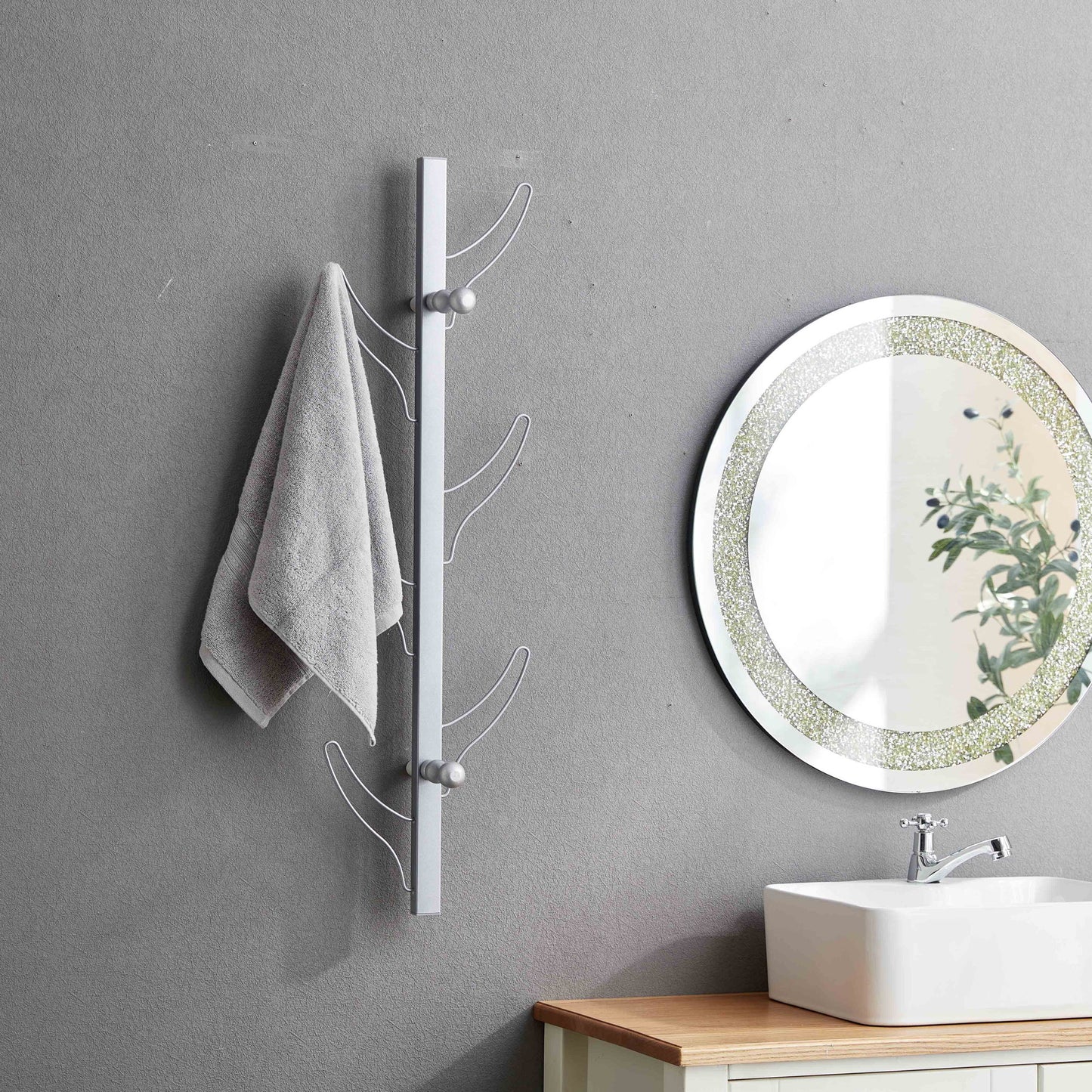 A gray towel hangs on the Vertical Eight Hook Coat Rack Wall Mount beside a round mirror with a decorative border above a white sink and wooden countertop in a bathroom with gray walls.