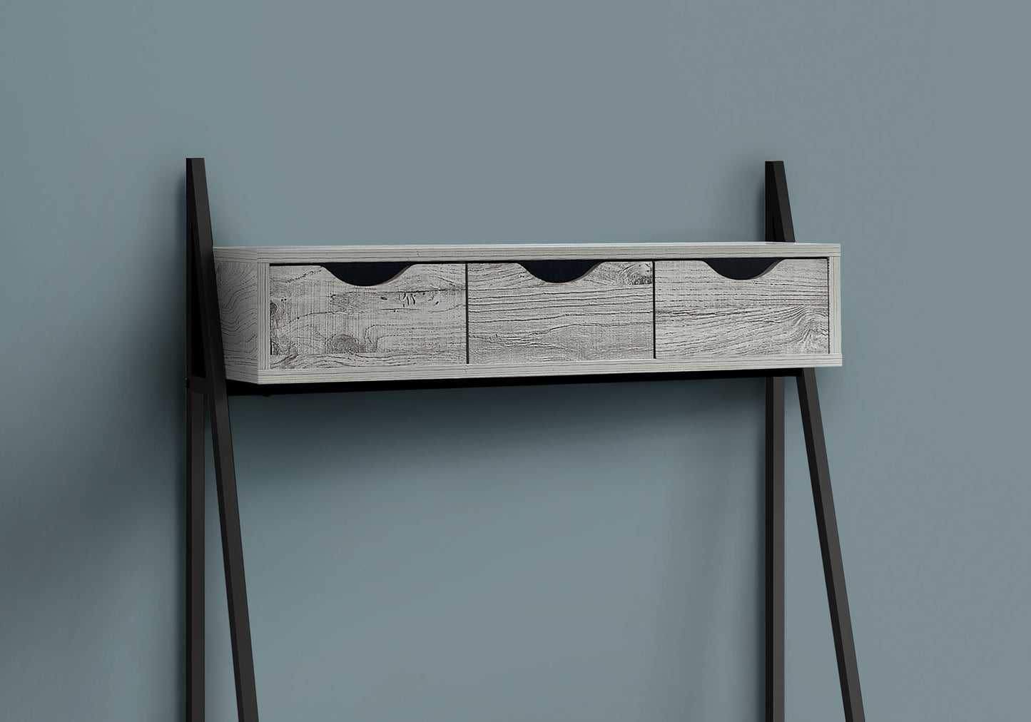 A Computer Desk for Home Office with three light wood storage drawers and black handles, featuring angled black metal legs, presents a contemporary and modern look against a plain blue-gray wall.