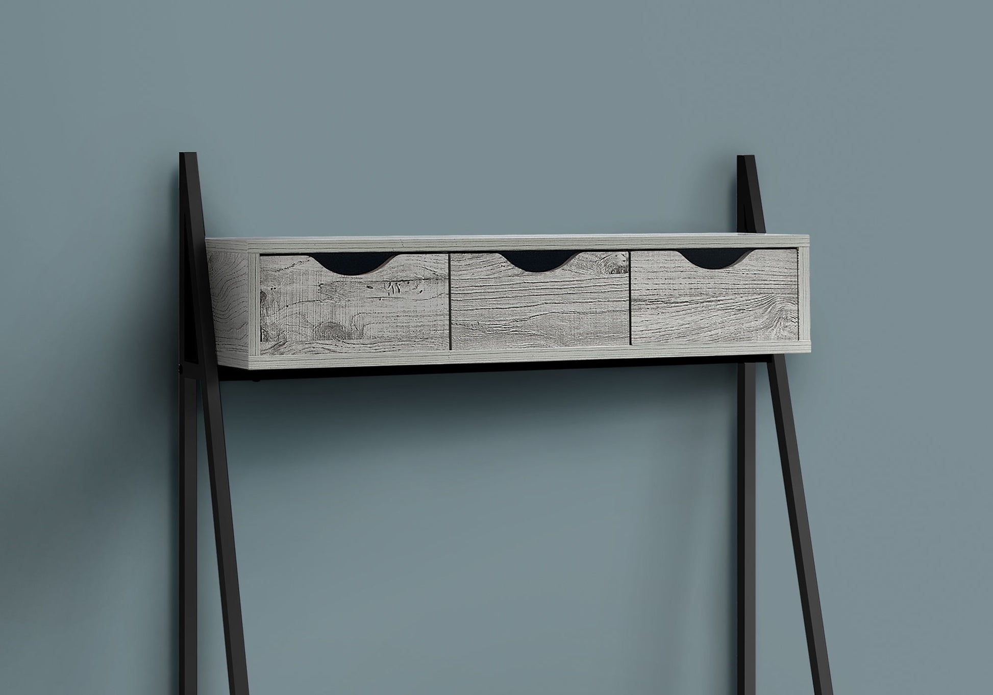A Computer Desk for Home Office with three light wood storage drawers and black handles, featuring angled black metal legs, presents a contemporary and modern look against a plain blue-gray wall.