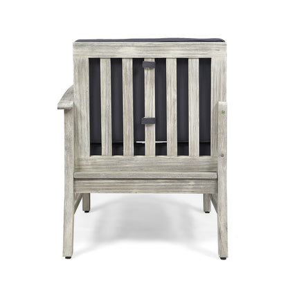 The Perla - Armchair is a wooden chair with a weathered gray finish, seen from the back, featuring vertical slats and a dark cushion attached to its backrest.