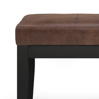 Close-up of the Lacey - Upholstered Tufted Ottoman Bench featuring a cushioned brown faux leather seat and black wooden legs, set against a white background.