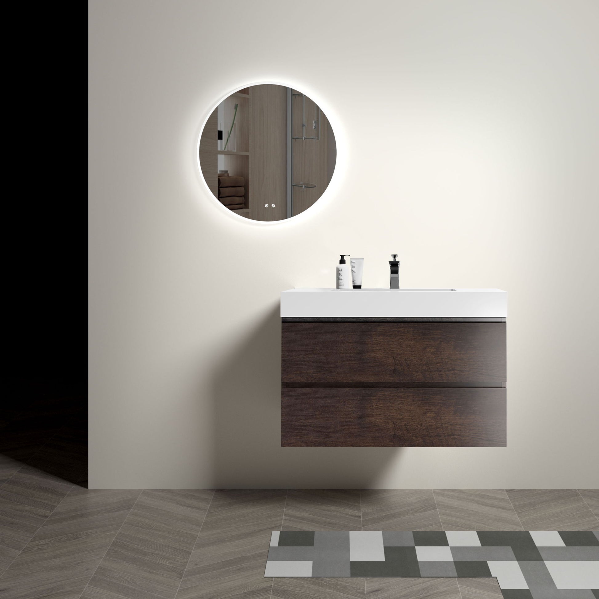 A modern bathroom with a round backlit mirror above the Alice wall-mounted floating vanity with a one-piece white sink. Two soap dispensers sit on the vanity, and patterned gray and beige tiles cover the floor.
