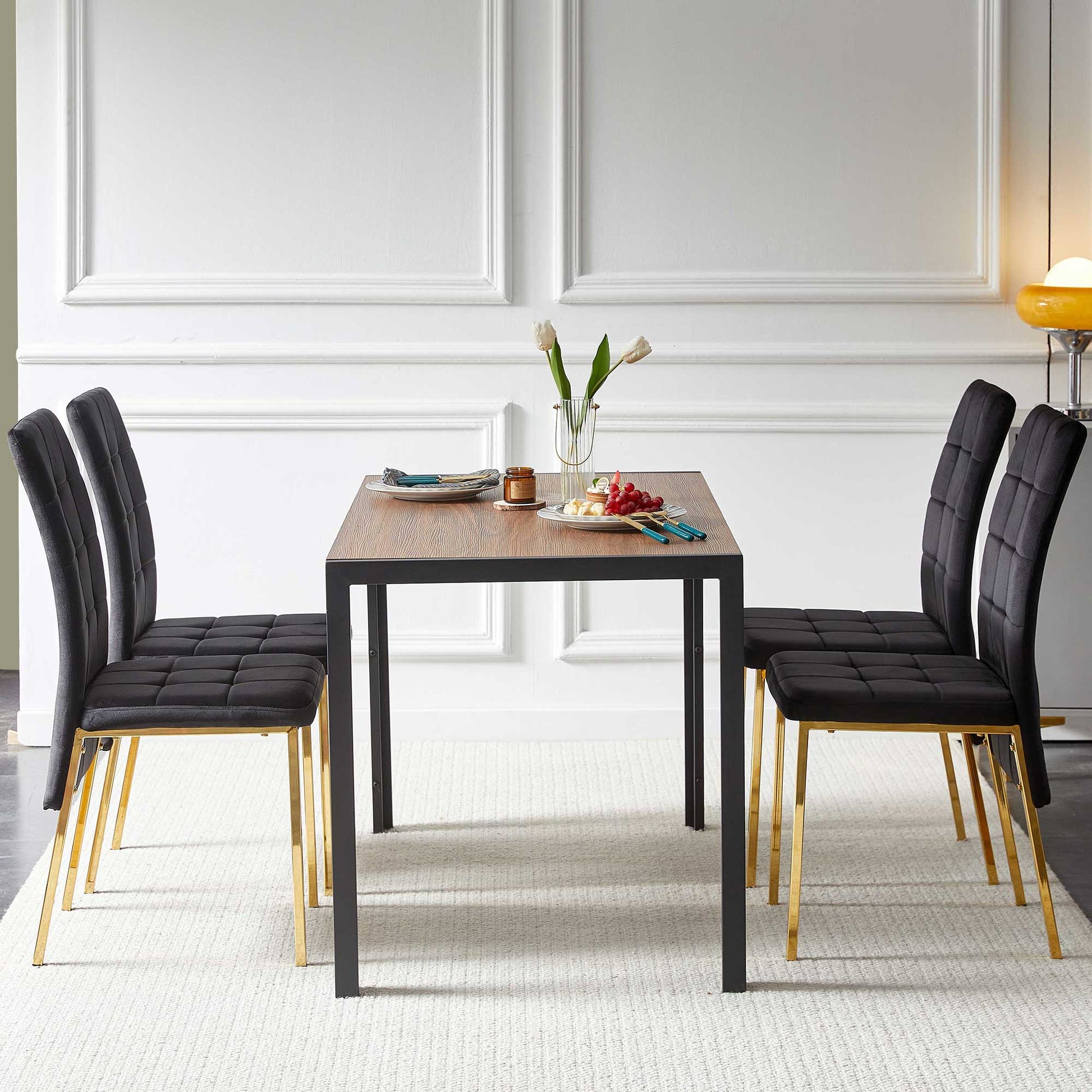 A modern dining room showcases a 5-piece set with a creative design dining table and four velvet high-back Nordic chairs featuring golden legs, set with plates, cups, utensils, a vase of white tulips, and a fruit plate.