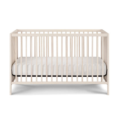 The Pixie Zen 3-in-1 Crib in walnut features vertical slats on all sides and includes a white mattress, displayed against a plain white background.