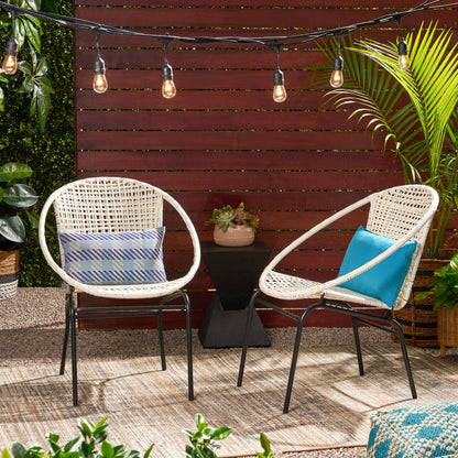 Two Java Chairs With Comfortable Design and cushions sit on a rug outdoors. String lights are above, with potted plants and a wooden privacy fence in the background.