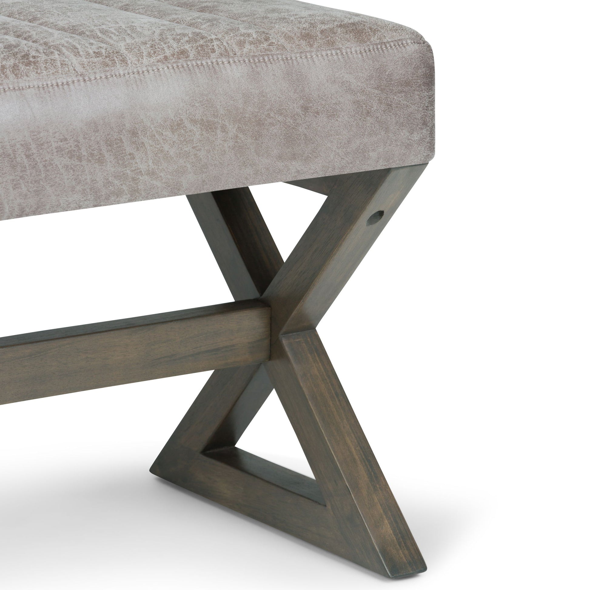 A close-up of the Salinger - Large Upholstered Ottoman Bench shows its light taupe cushion and dark wooden X-shaped leg, set against a white background.
