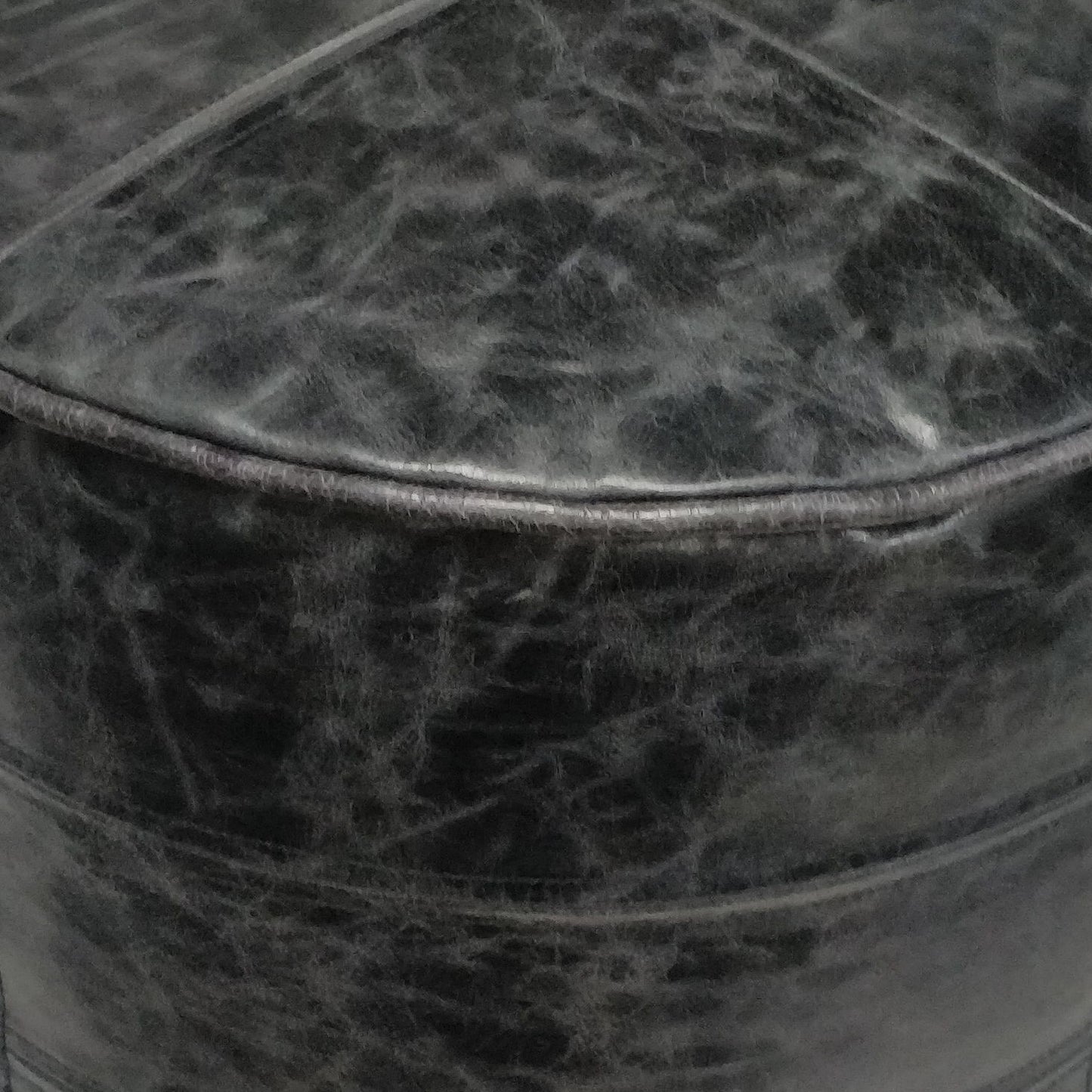 Close-up of the Connor Handcrafted Round Pouf's black leather surface, highlighting creases, stitching, a rounded edge, and its textured, worn appearance.