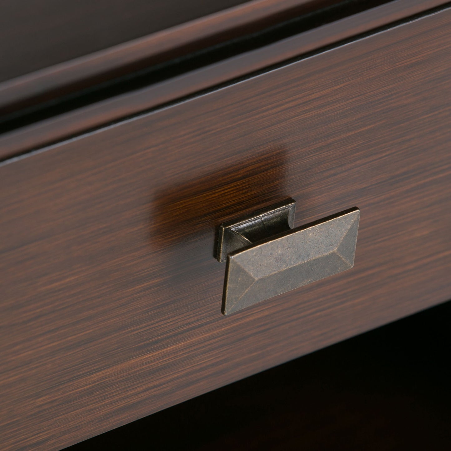 Close-up of the Artisan - Handcrafted Bedside Table’s dark wooden drawer, featuring a rectangular faceted metal handle in antique brass and a subtly grained wood surface.