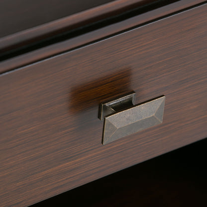 Close-up of the Artisan - Handcrafted Bedside Table’s dark wooden drawer, featuring a rectangular faceted metal handle in antique brass and a subtly grained wood surface.