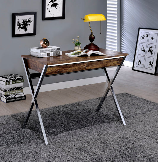 The Callers Weathered Writing Desk in Chrome and Oak features on a gray rug with an open book, potted plant, golden lamp, and decorative clock on top. Abstract wall art and a stack of books complete the modern room decor.