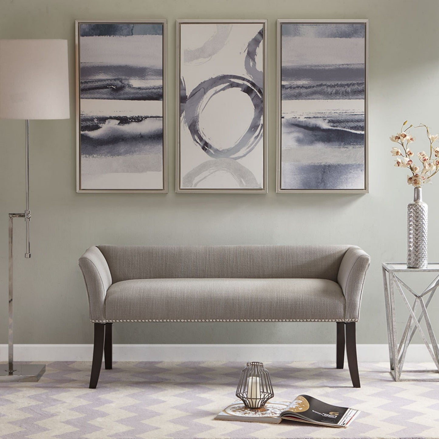 A modern living room featuring the Elegant Design Bench Upholstery with a solid wood frame, three abstract paintings, a floor lamp, glass side table with a vase, plus a magazine and candle holder on a patterned rug.