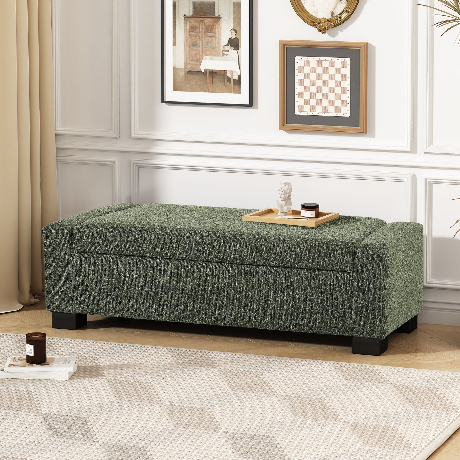 A Textured Fabric Ottoman Bench With Hinged Lid in green sits against a white wall with framed art and beige curtains in a bright living room. On top of the bench are a tray, book, and candle.