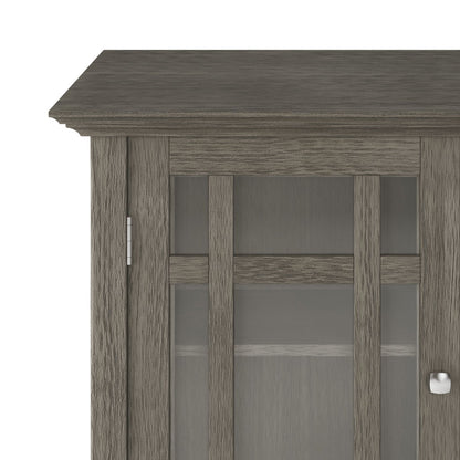Partial view of Bedford - Storage Media Cabinet in gray wood, featuring a glass-paneled door with metal knob, modern design, visible wood grain texture, and an interior shelf.