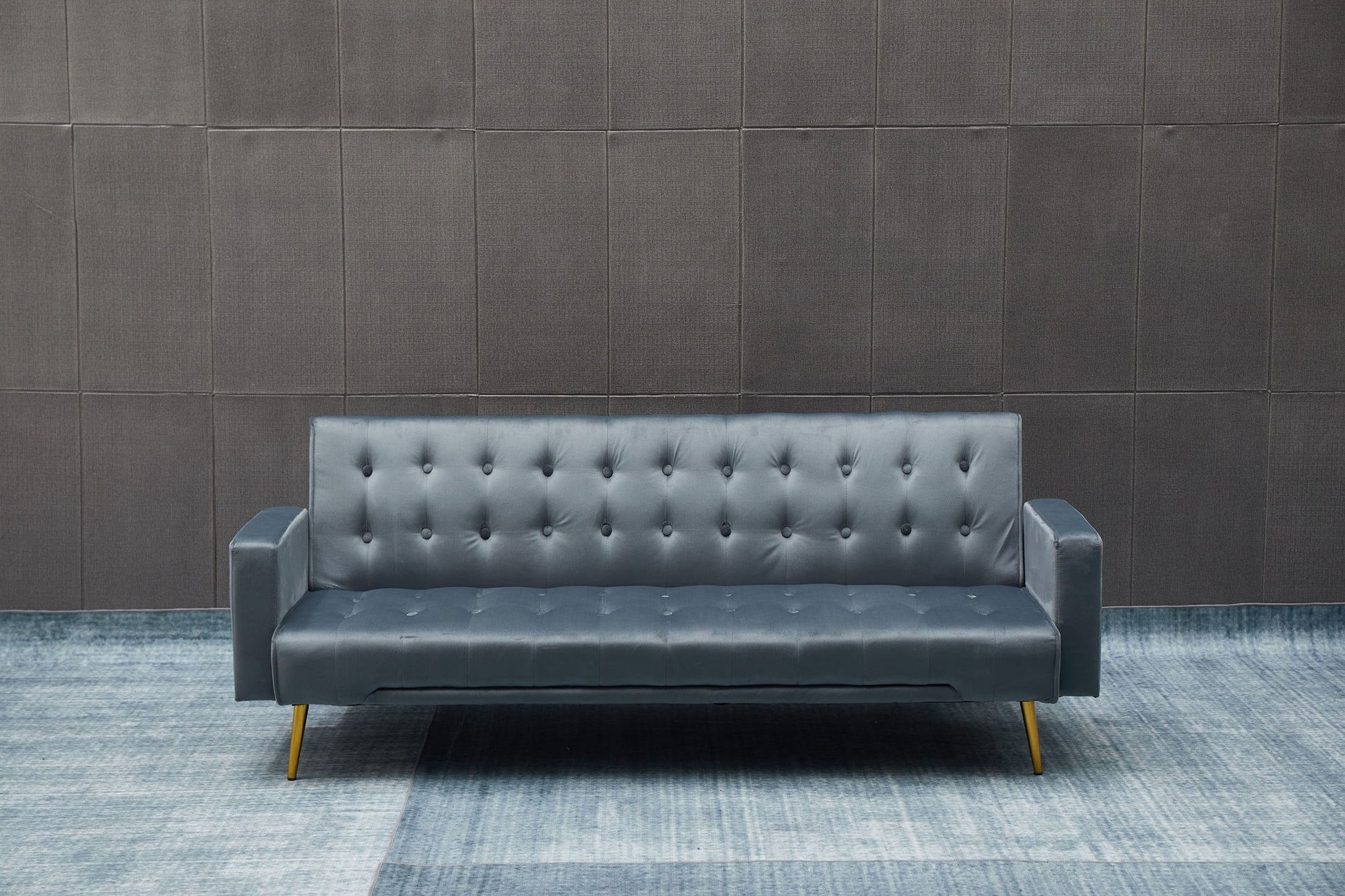 The Comfort Compact Design Sofa Bed, in modern dark gray with gold legs, is placed on a blue patterned floor before a textured dark wall.