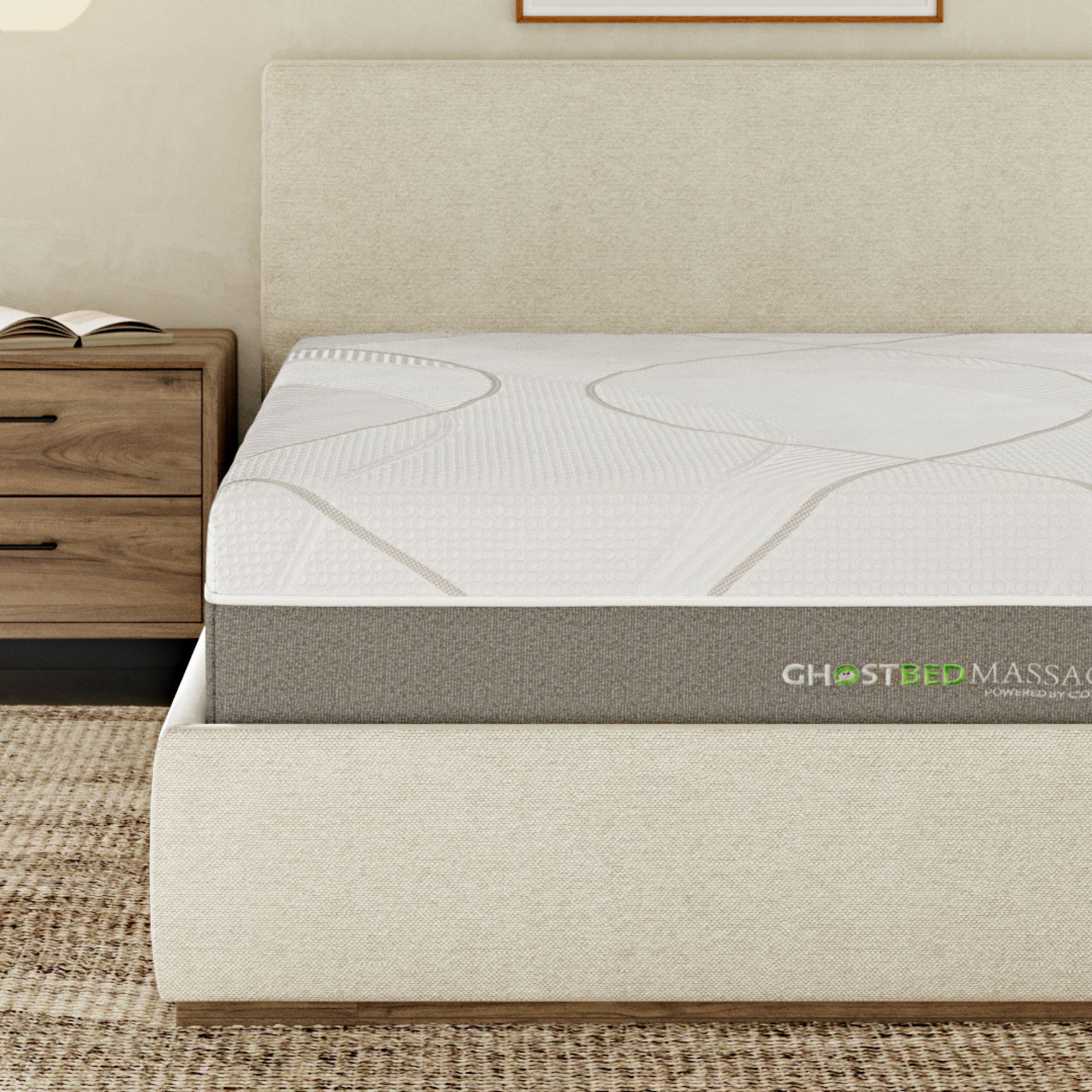 A modern bedroom features a beige upholstered bed with a 12" Profile Massage Mattress Hybrid, next to a wooden nightstand with drawers, on a textured rug.