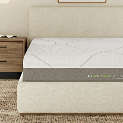A modern bedroom features a beige upholstered bed with a 12" Profile Massage Mattress Hybrid, next to a wooden nightstand with drawers, on a textured rug.