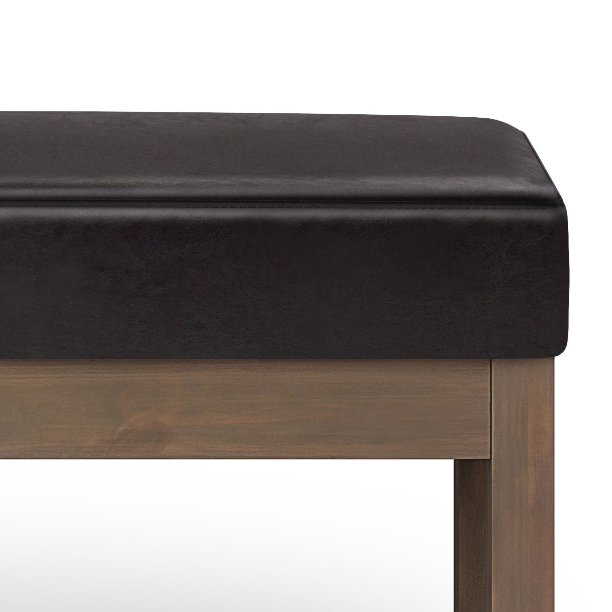 A close-up of the Milltown - Upholstered Ottoman Bench shows its dark brown cushioned seat and wooden frame with straight legs, set against a white background.