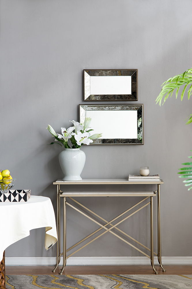 A modern entryway features a narrow console table with a white vase of lilies, candle, and decor. Two Antique Rectangle Mirrors With Floral Accents hang above on the gray wall, complementing the scene with elegance.