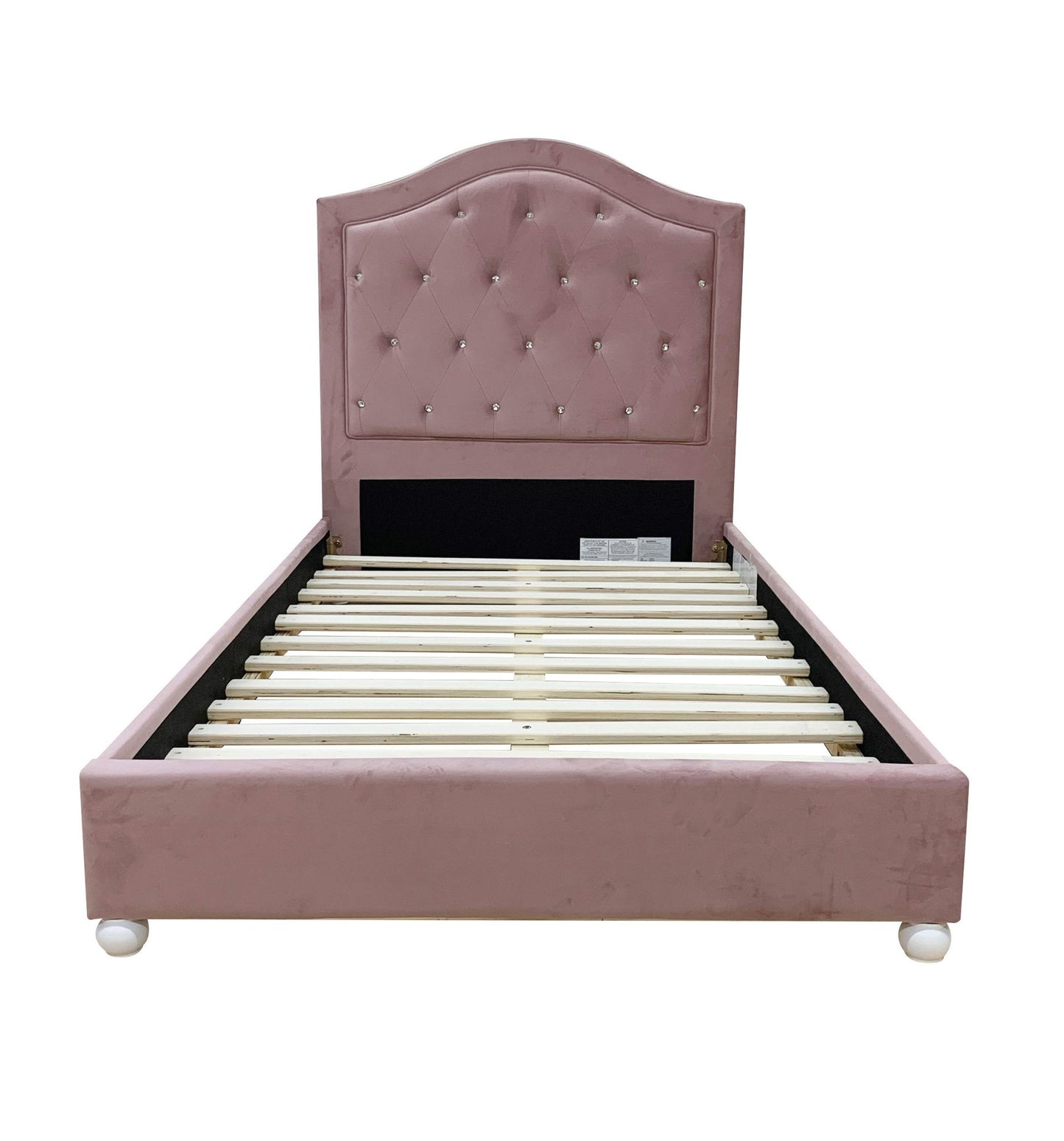 The Reggie Twin Bed in pink features a tufted headboard, soft velvet-like upholstery, wooden slats, and short round feet. Shown from the front against a white background.