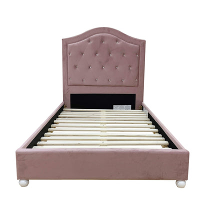 The Reggie Twin Bed in pink features a tufted headboard, soft velvet-like upholstery, wooden slats, and short round feet. Shown from the front against a white background.