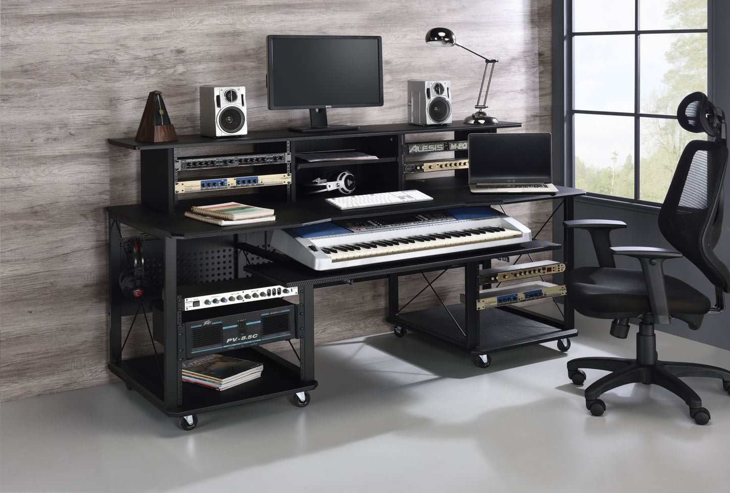 The Megara Music Desk features multiple storage options, a spacious workspace for keyboard, monitor, speakers, and audio gear, plus room for an office chair—all beside a tall window and set against a wood-paneled wall.