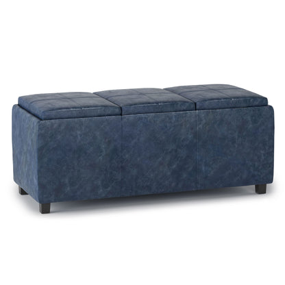 The Avalon Upholstered Storage Ottoman is a rectangular, blue bench with three cushioned sections, short black legs, and hidden storage, shown on a white background.