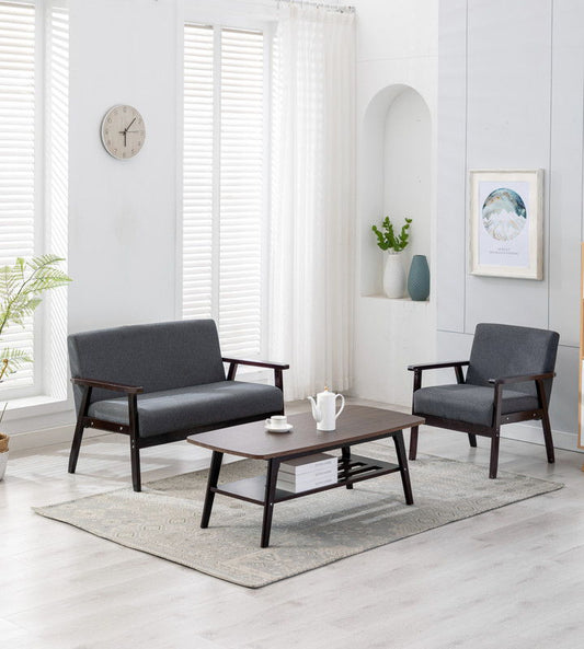 The Bahamas Living Room Set features a dark wood coffee table, gray love seat and armchair, light walls, large windows with white curtains, a potted plant, wall clock, and framed art for a modern touch.