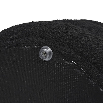 Close-up of the Fuji - Oversized Round Storage Ottoman, featuring black textured fabric and a clear plastic button sewn onto its edge.