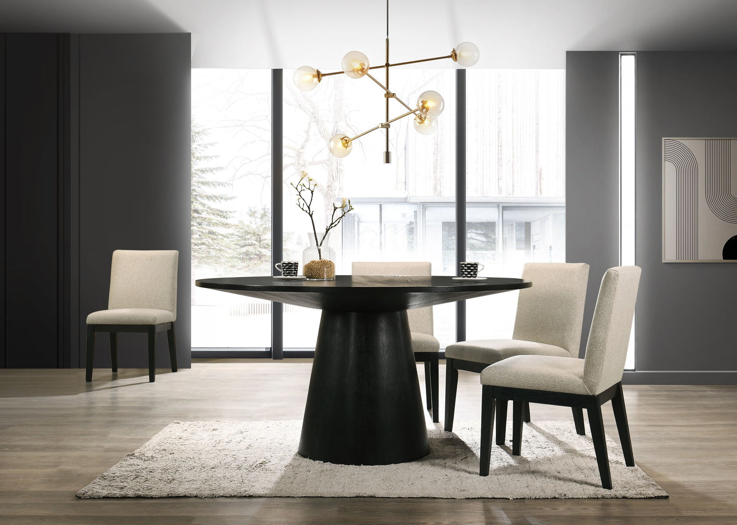 The Jasper Wide Contemporary Round Dining Table Set features a black table, four beige upholstered chairs, a white rug, gold chandelier, and large windows. Minimalist decor includes a vase with branches and abstract wall art.