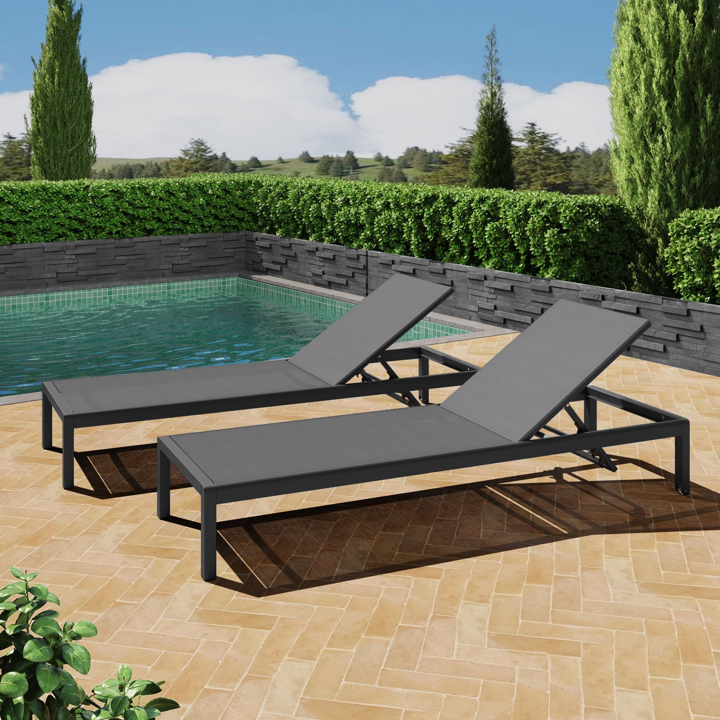 Two Outdoor Patio Chaise Lounges with 5 Reclining Positions sit side by side on a tiled patio near a pool, surrounded by green hedges, trees, and a stone wall under a blue sky with scattered clouds.