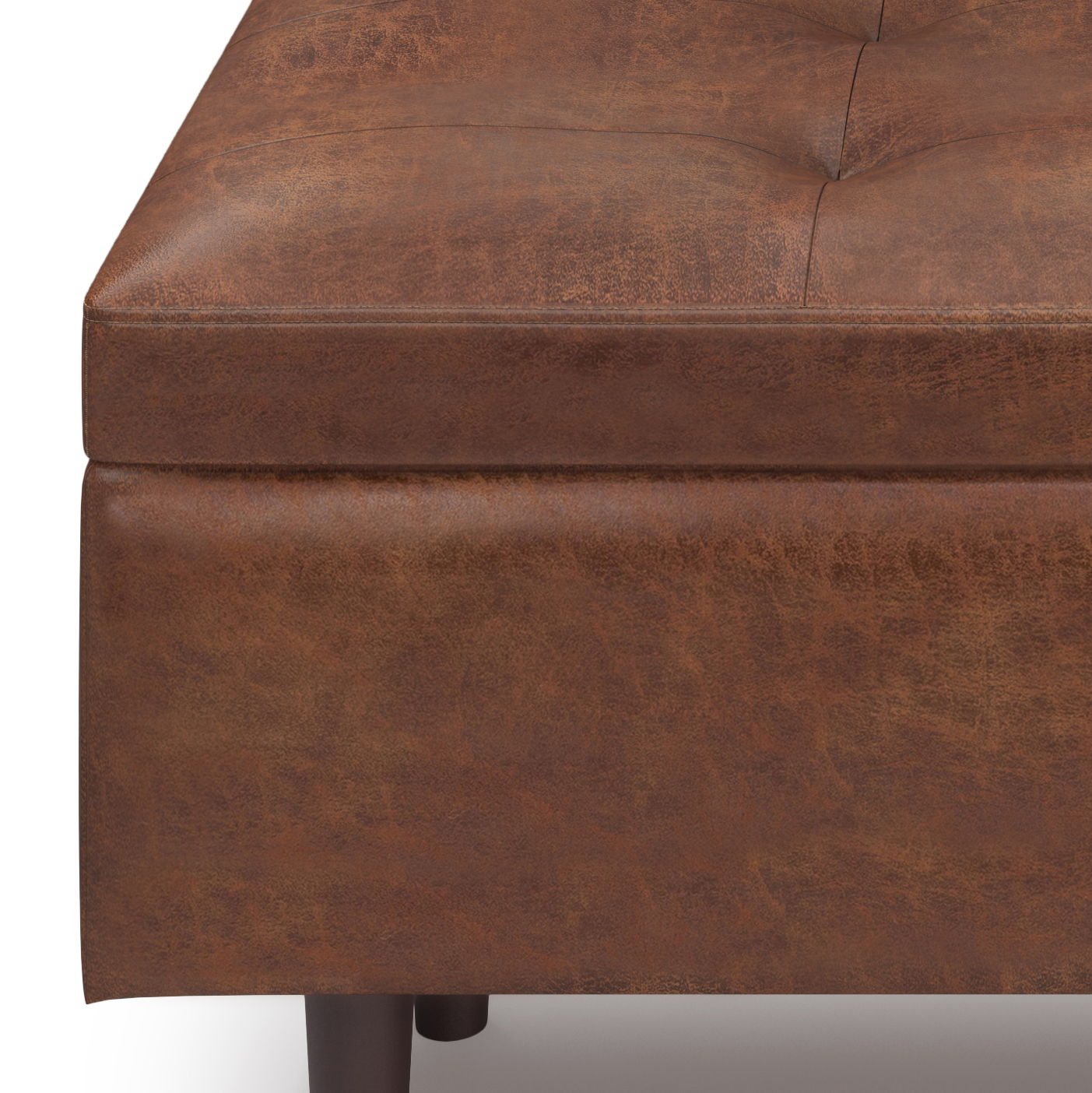 Close-up of the corner of the Shay Large Square Coffee Table Storage Ottoman in brown faux leather with tufted design, dark wooden legs, and visible texture and stitching details. Mid-century style.