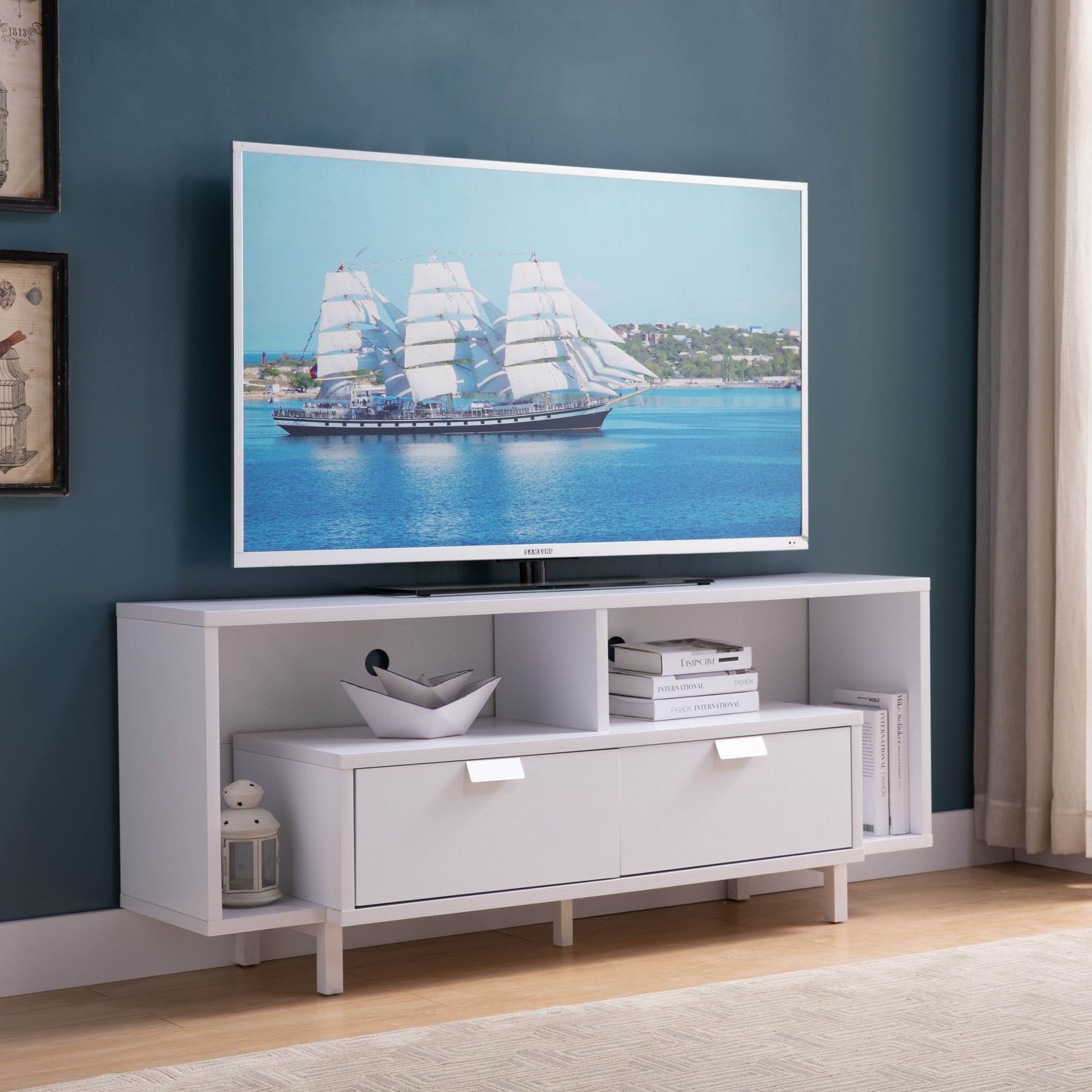 A flat-screen TV on the Modern TV Stand & Two Shelves And Two Drawers shows a sailing ship on blue water, with books, decor, and a lantern arranged on the stand, set against a blue wall.