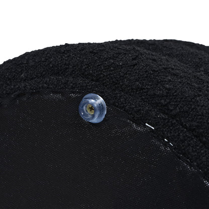 Close-up of a blue translucent button sewn onto the textured black fabric of the Fuji - Oversized Round Storage Ottoman, with visible stitching and soft, thick material.