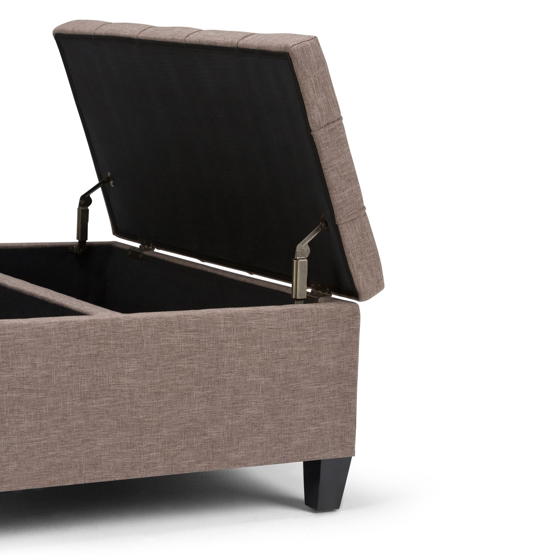 The Harrison Upholstered Coffee Table Storage Ottoman features a padded, rectangular design with a hinged lid that opens to reveal storage space. It is upholstered in light brown fabric and stands on short black legs.