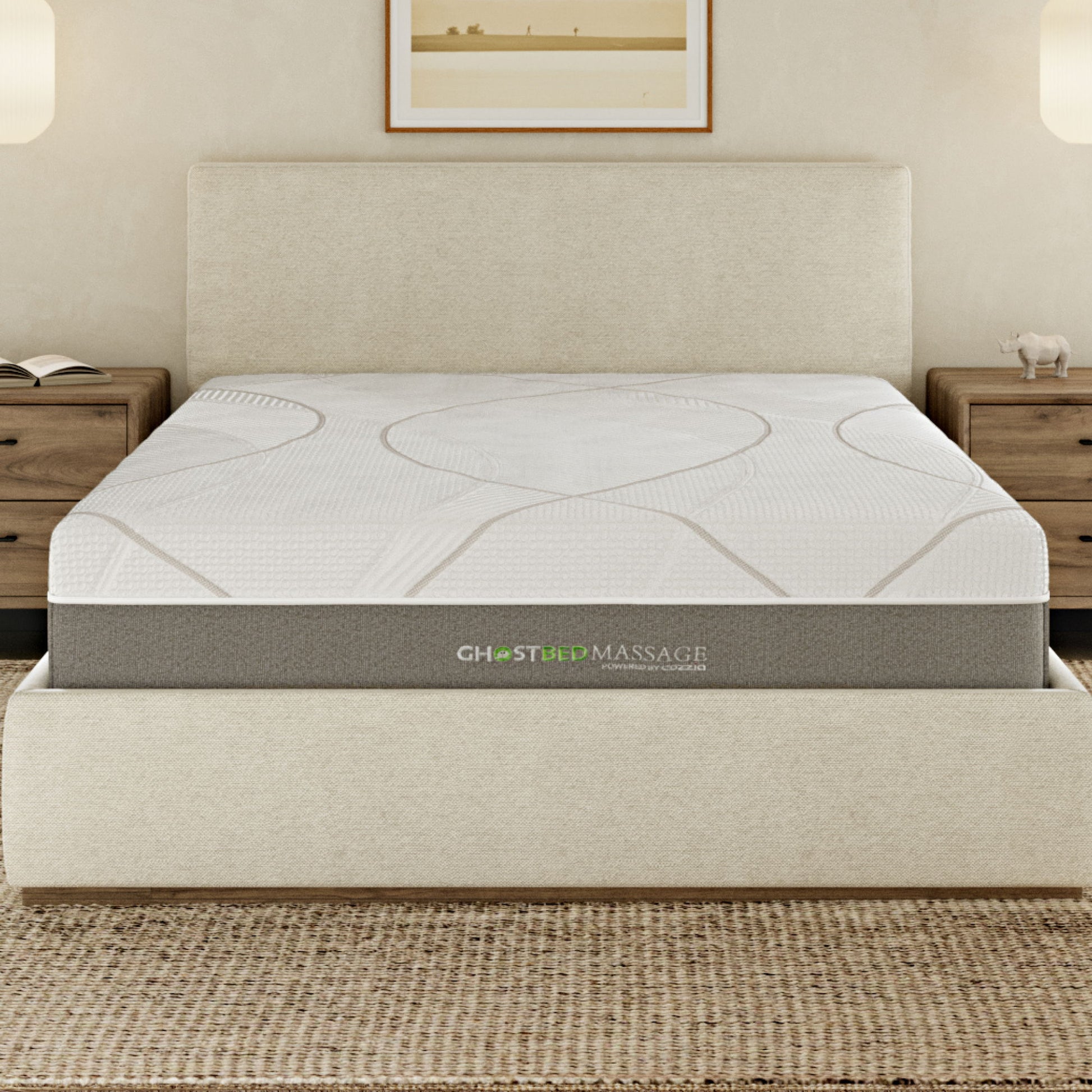 A neatly made bed features the 12" Profile Massage Mattress Hybrid on a cream-colored upholstered frame, flanked by wooden nightstands and lit by wall sconces. A framed picture hangs above the headboard.
