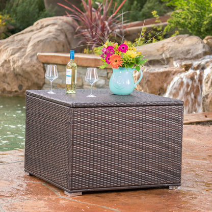 The Santa Rosa - Storage Table is styled with a bottle of wine, two glasses, and a turquoise pitcher of flowers, set next to a tranquil garden waterfall and pond.