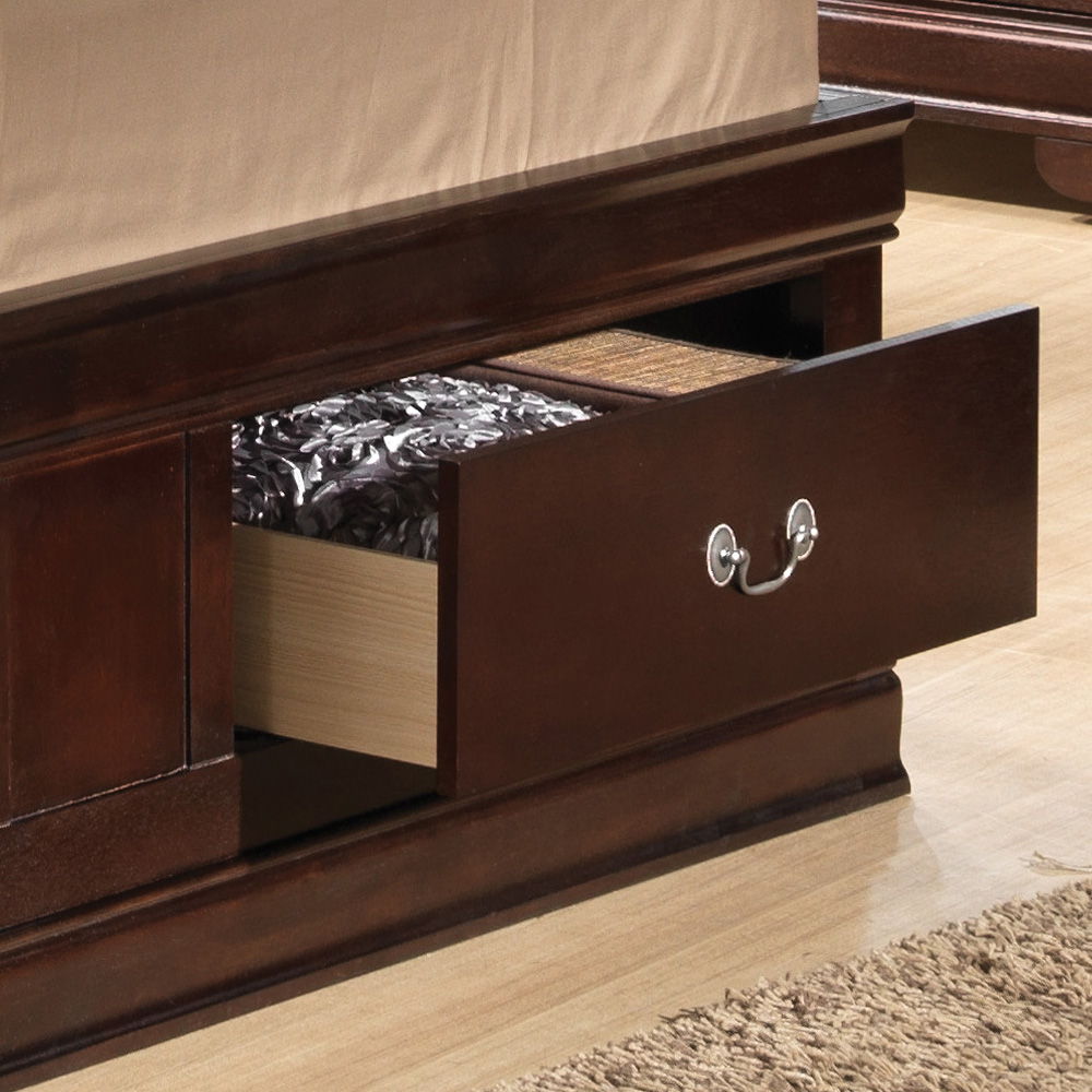A close-up of the Louis Phillipe - Bookcase Storage Bed shows its dark wood frame with an open underbed drawer, a mattress topped with a floral cover, light wooden flooring, and part of a textured beige rug in view.