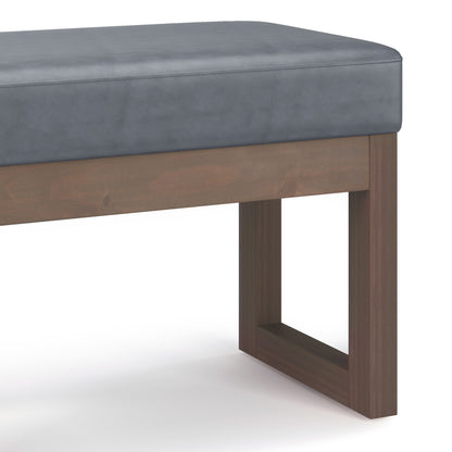 A close-up of the Milltown - Upholstered Ottoman Bench featuring a gray cushioned seat and a rectangular wooden base with clean lines, set against a white background.