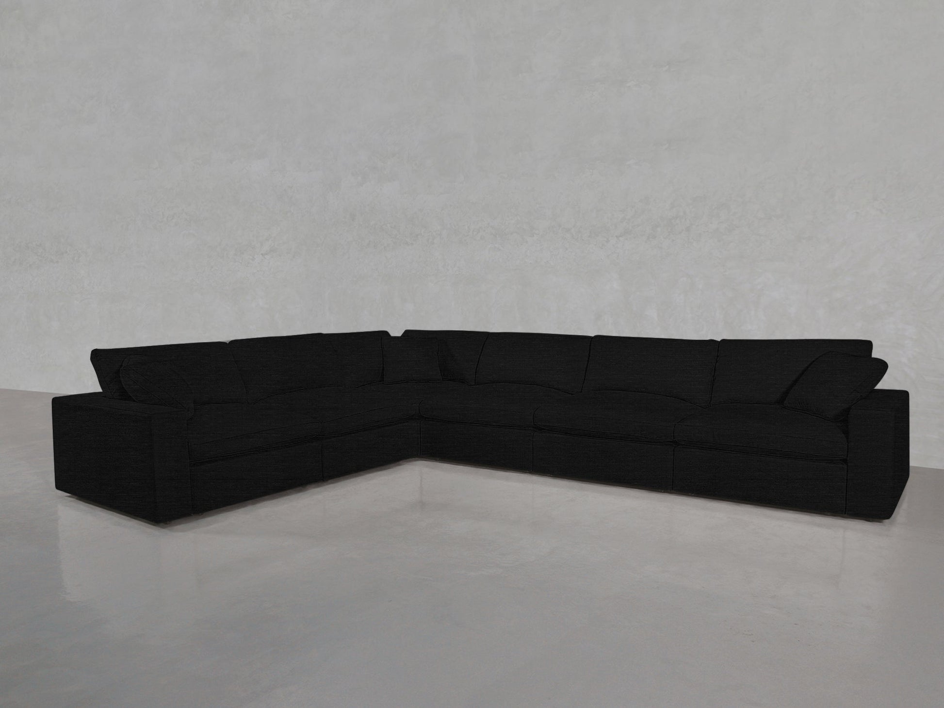 The 6-Seat Modular Corner Sectional in black, with wide armrests and plush cushions, is arranged in an L-shape on a shiny light gray floor against a plain, light-colored wall.