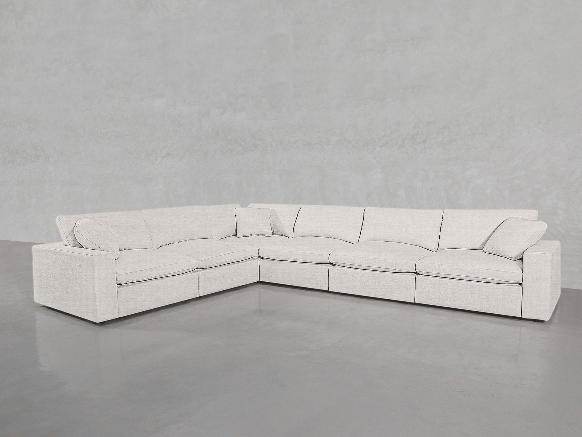 A 6-Seat Modular Corner Sectional, upholstered in light beige fabric, sits on a smooth gray concrete floor against a pale gray textured wall.