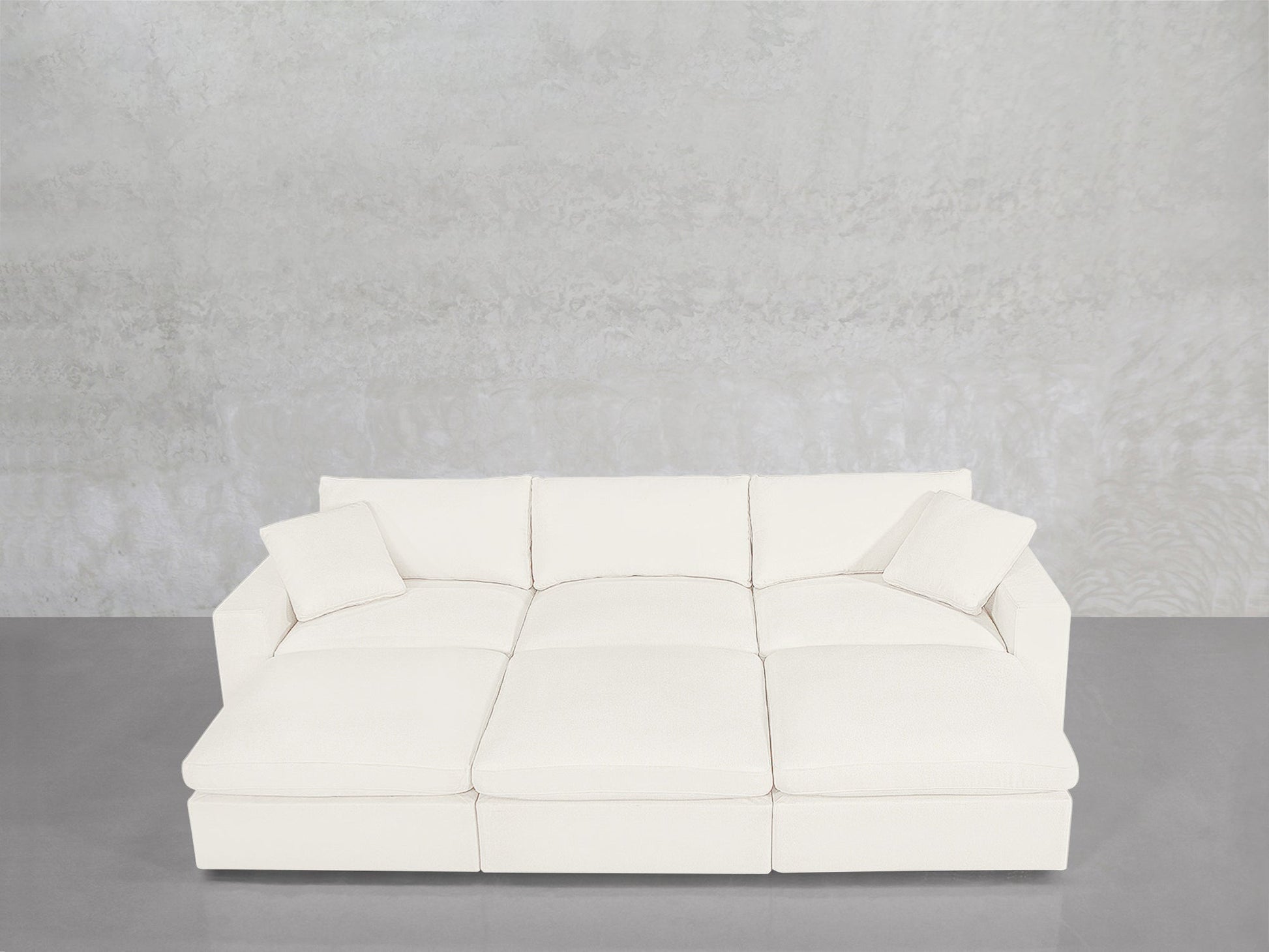 A contemporary 6-Seat Modular Daybed with matching cushions is arranged against a light gray textured wall and a smooth gray floor.